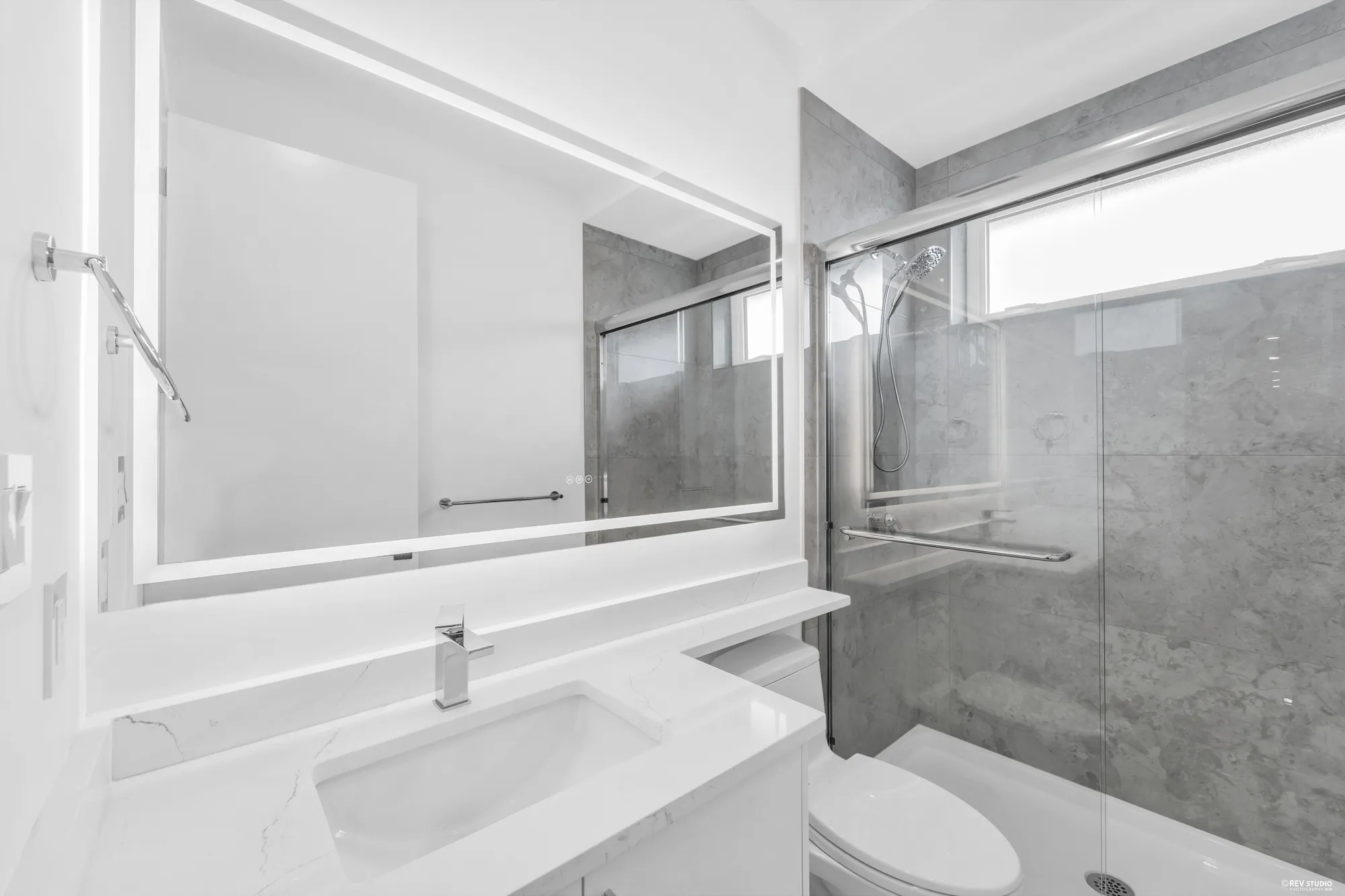 A bathroom with a walk-in shower behind glass and a window above the vanity
