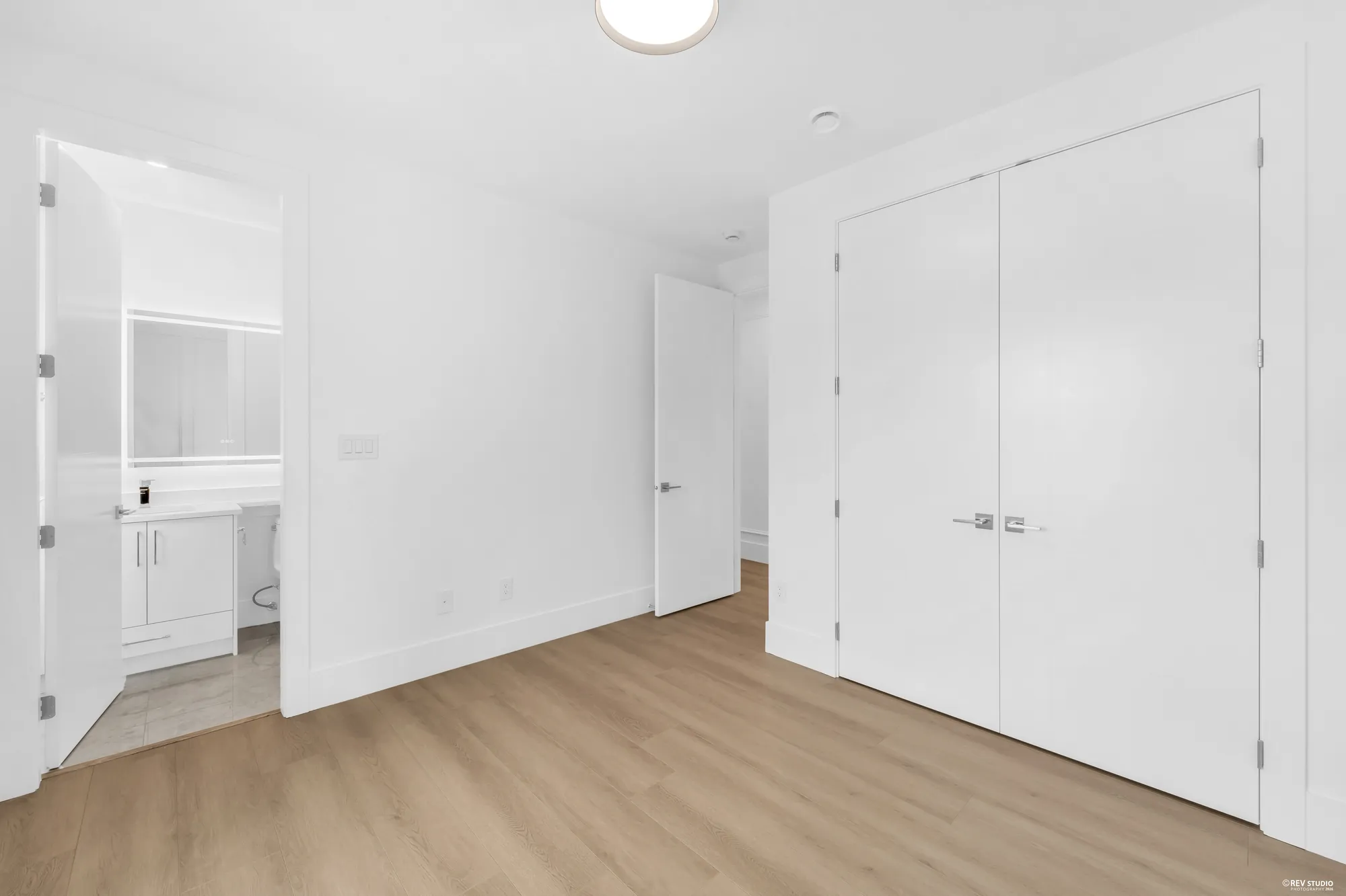 An unfurnished bedroom with a double closet and its bathroom visible through the door