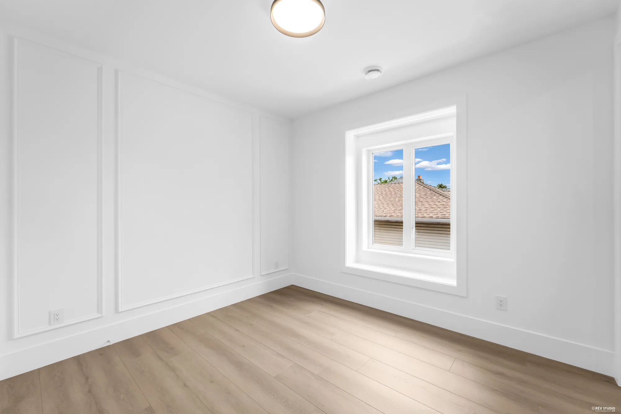 An unfurnished bedroom with the window in the corner and wainscot below it