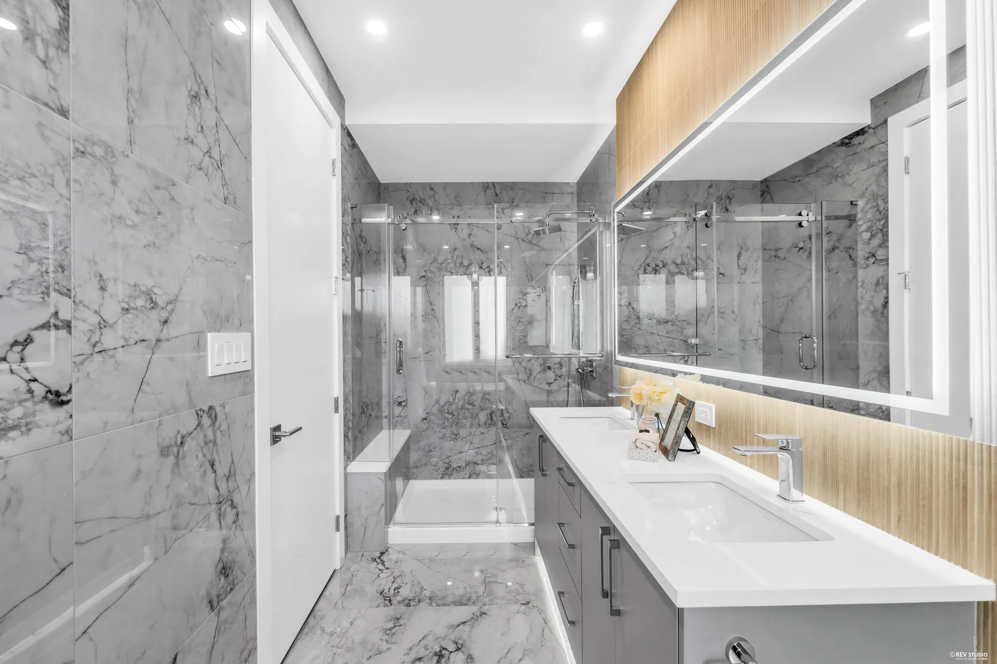 The same bathroom from the tub end, marble to the ceiling and a lit mirror