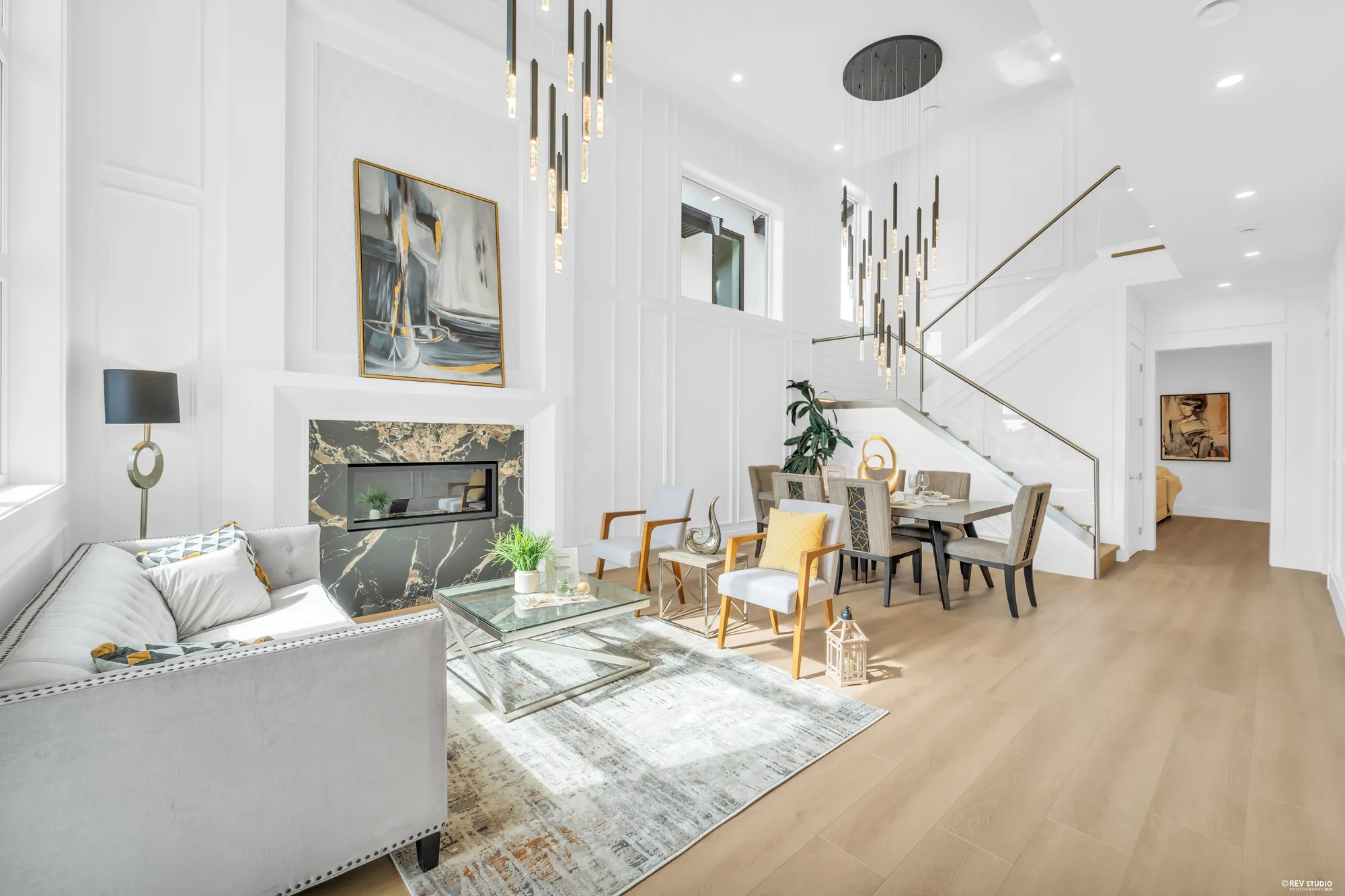 The double-height room at the entry, panelled walls, a long drop of pendant lights and the stair beyond