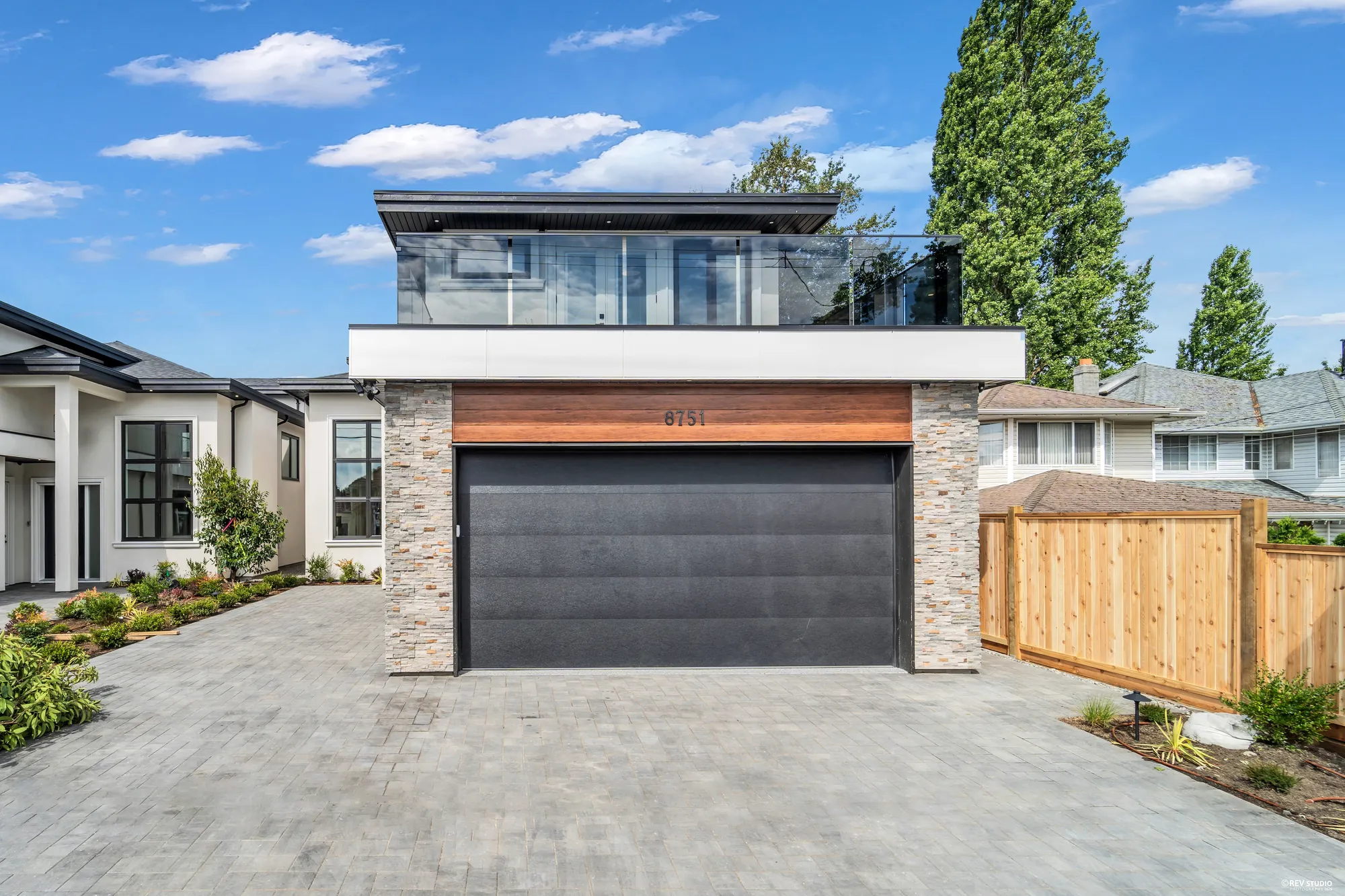 The front of the house seen square on from the driveway, garage door in the middle and the deck above