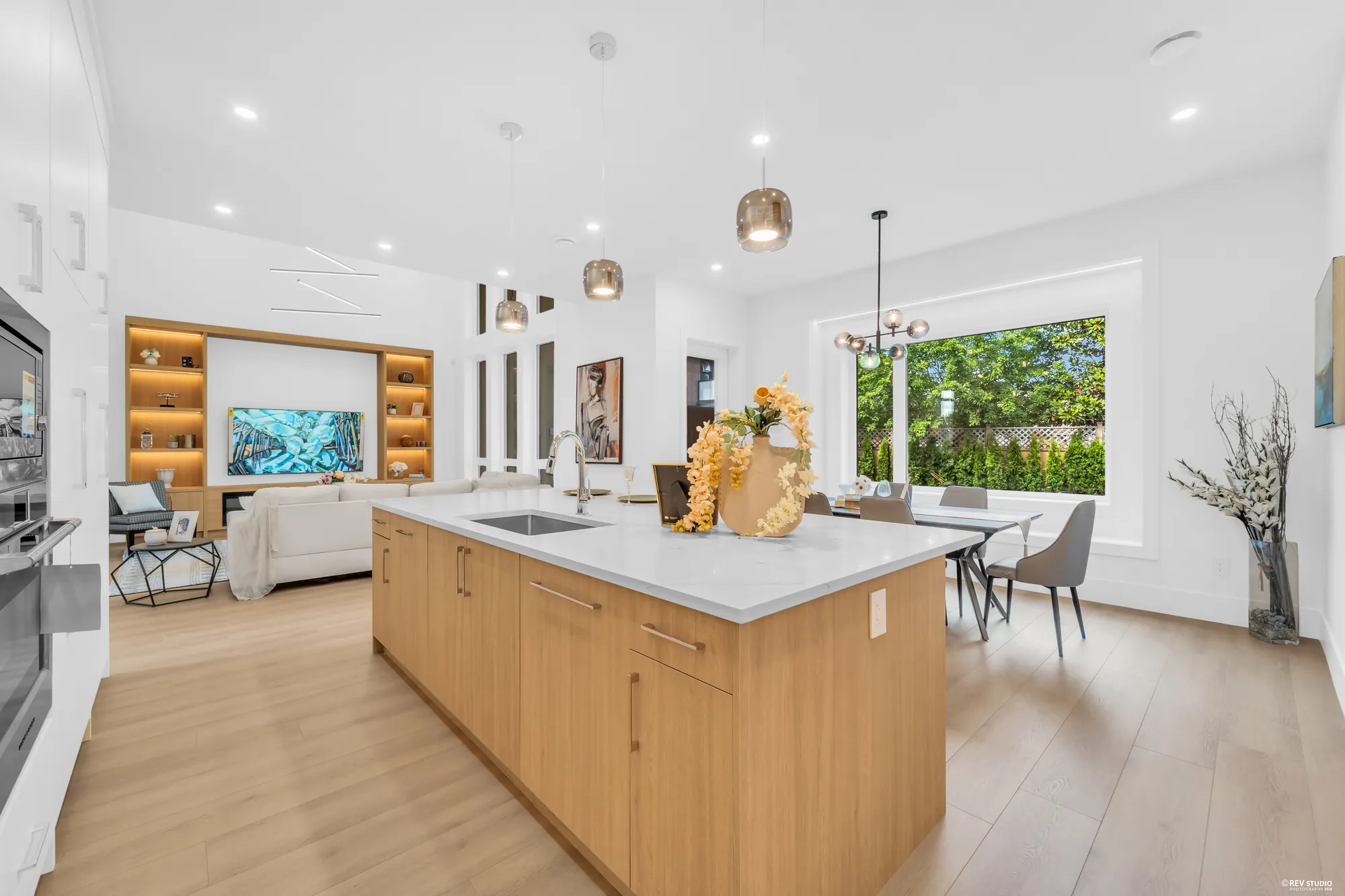The kitchen island in oak with a white counter, cabinets and ovens along the far wall