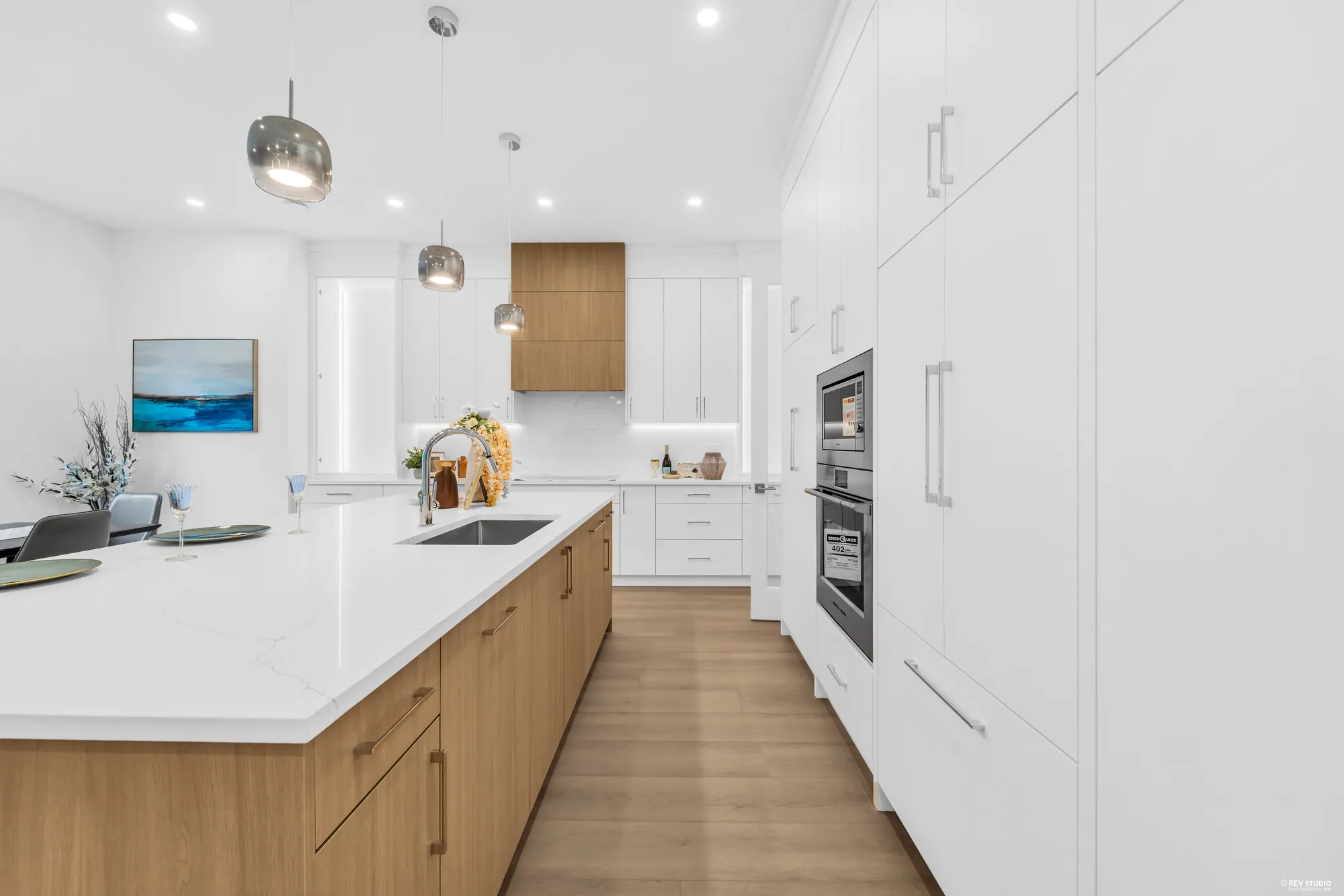 The run of tall white cabinets with the wall ovens and a screen above the counter