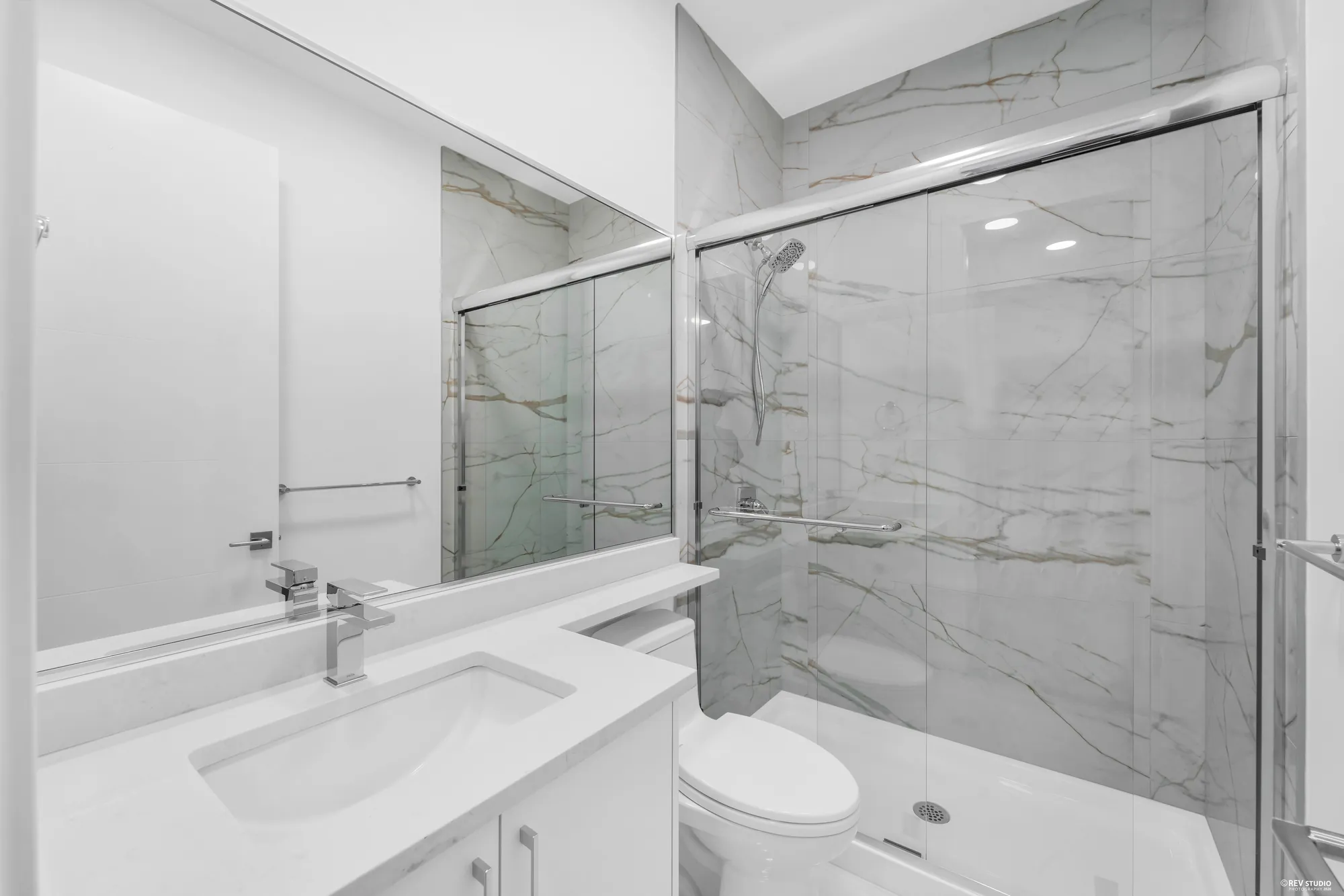 A bathroom with a tub and shower behind glass, marble to the ceiling