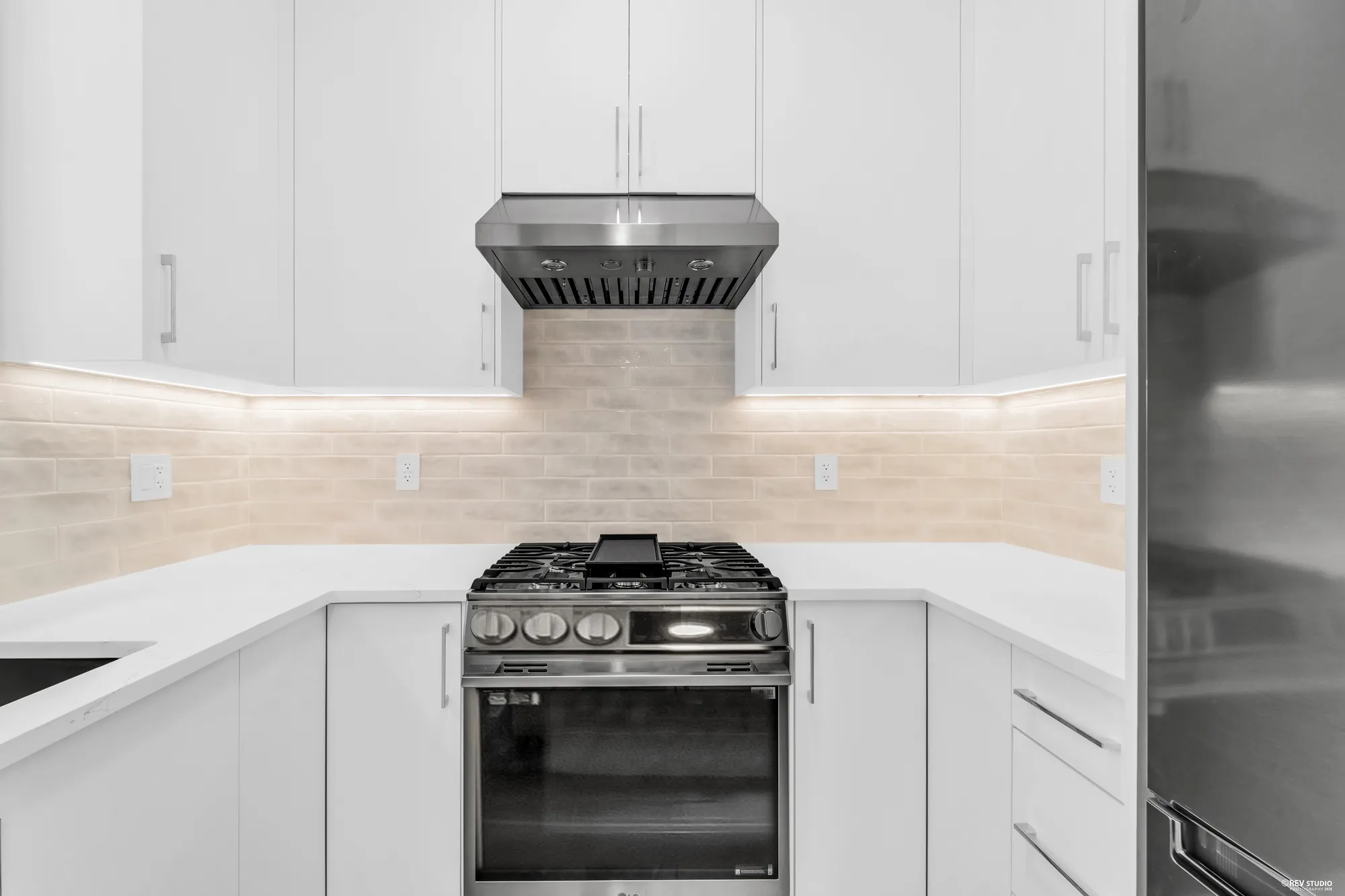 The wok kitchen: gas range, stainless hood, tiled splashback and a tall fridge